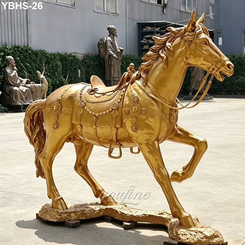 A golden bronze horse statue with intricate saddle decorations, displayed outdoors. The statue stands on a textured base in detail.