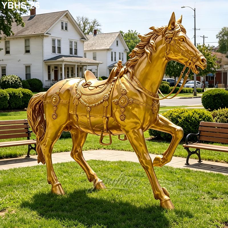 A stunning golden bronze horse statue with intricate saddle details placed in a grassy park surrounded by benches and houses.