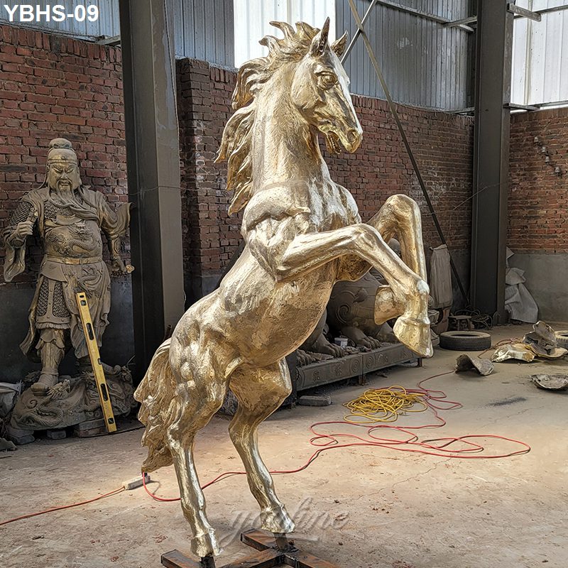 A detailed golden bronze horse statue in a rearing pose, situated in a workshop with brick walls, tools, and sculptural elements around.