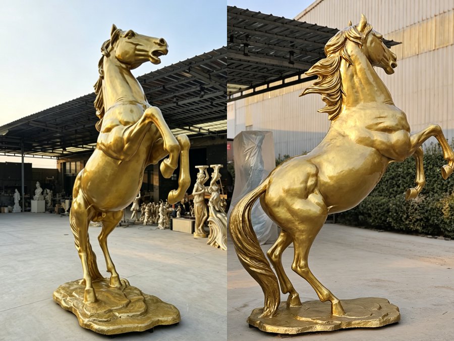Golden bronze horse statue in rearing pose on a textured base, displayed outdoors near other sculptures under a covered area.