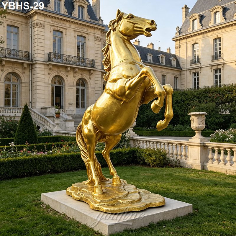 A majestic golden bronze horse sculpture rearing on a decorative base, placed in the landscaped garden of a stately manor.