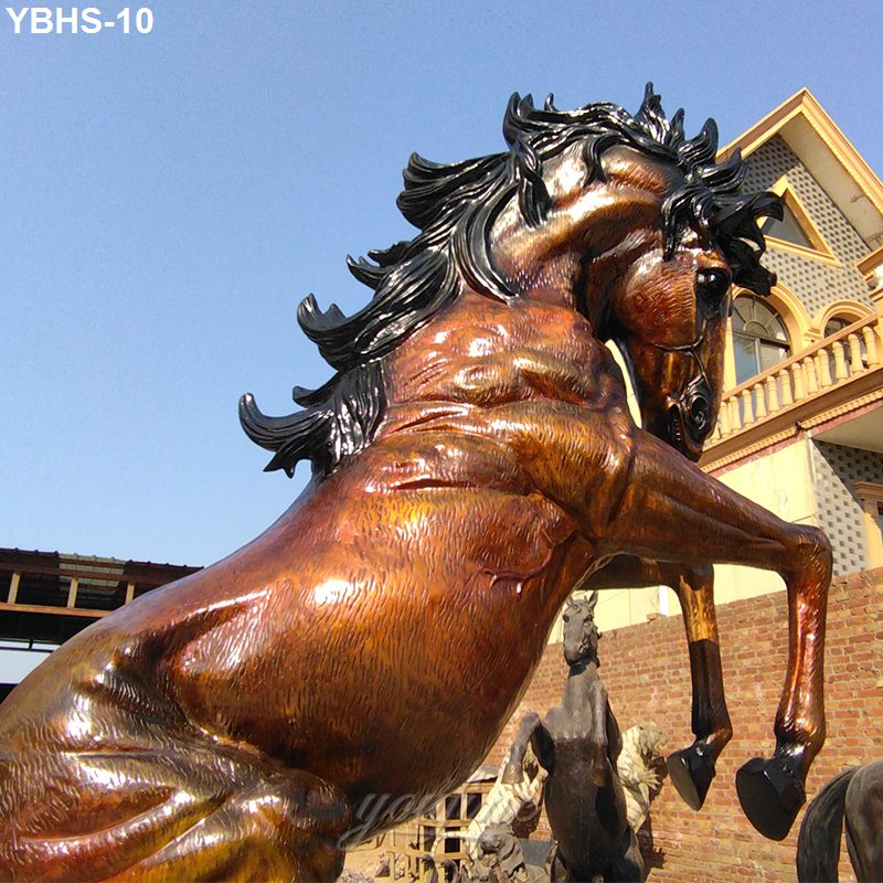 Detailed bronze sculpture of a rearing horse with flowing mane, showcased outdoors near a traditional building with arched windows.