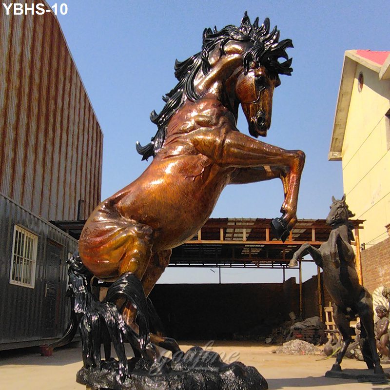 Large bronze sculpture of a rearing horse with flowing mane displayed outside a workshop with rustic and modern structures visible.