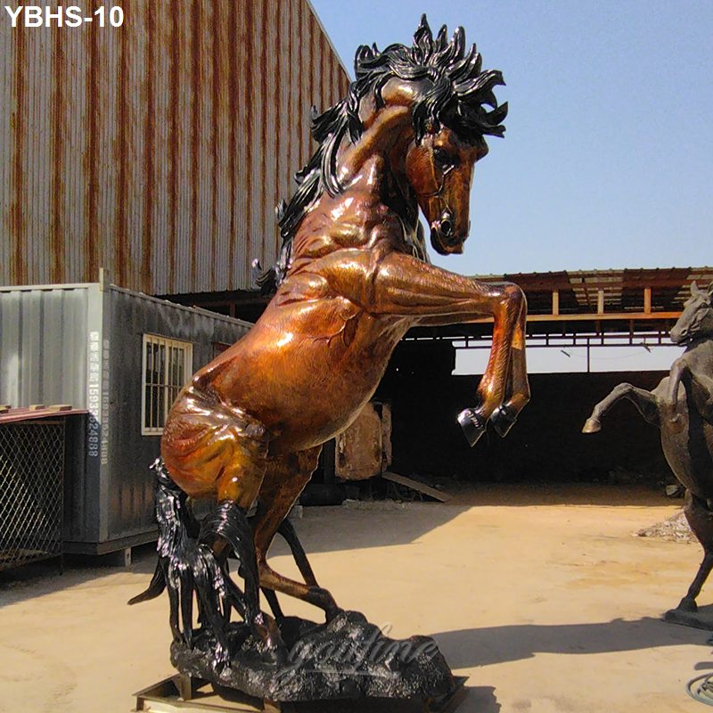 Detailed bronze sculpture of a rearing horse with a polished finish, displayed outdoors near industrial structures.
