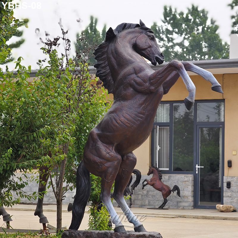 Bronze horse statue depicting a rearing stallion in an outdoor setting, surrounded by greenery and placed near a modern building facade.