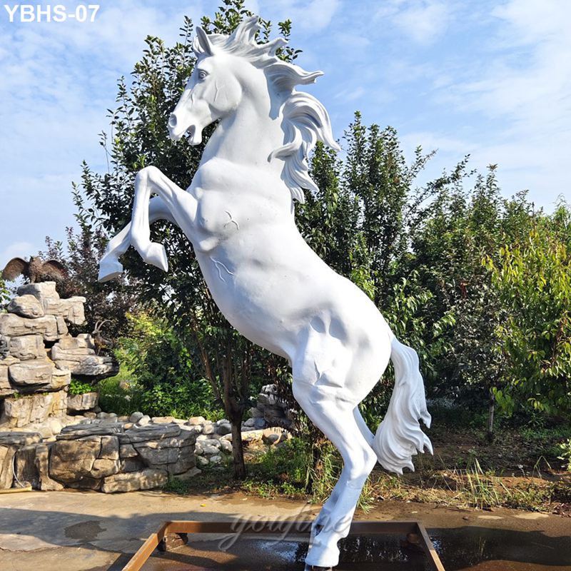 A white horse sculpture in a majestic rearing pose, surrounded by greenery and set against a blue sky in a landscaped garden.