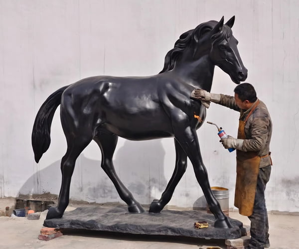 Hand wax sealing a finished bronze horse