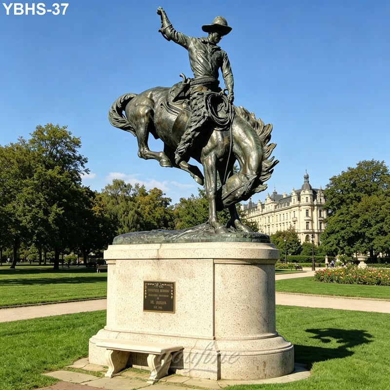 Bronze sculpture of a cowboy riding a rearing horse, mounted on a stone pedestal in a landscaped park with a historic building in the background.