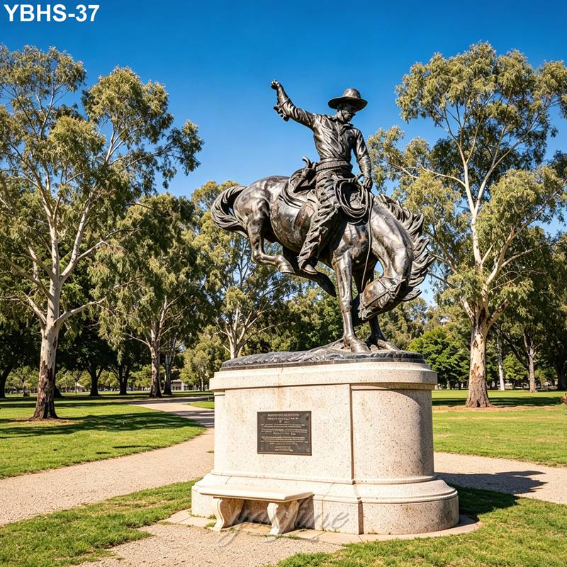 Bronze statue of a cowboy riding a rearing horse on a stone pedestal, surrounded by trees and pathways in a park.