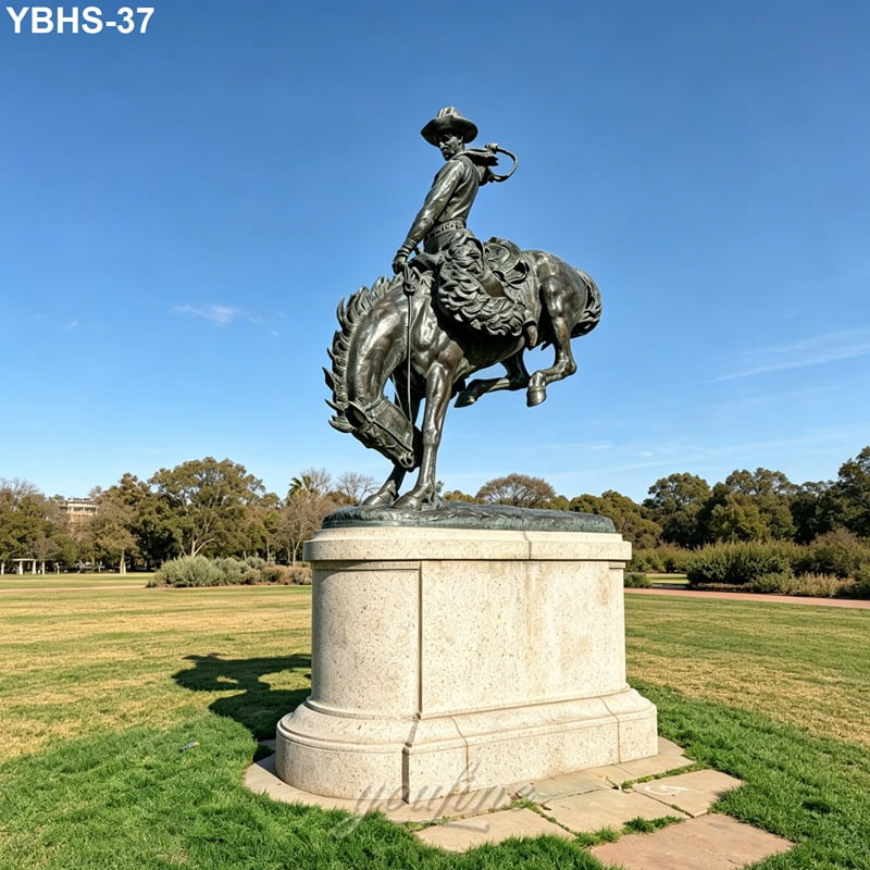 Bronze statue of a cowboy on a rearing horse atop a stone pedestal in a manicured park with trees and open grass.