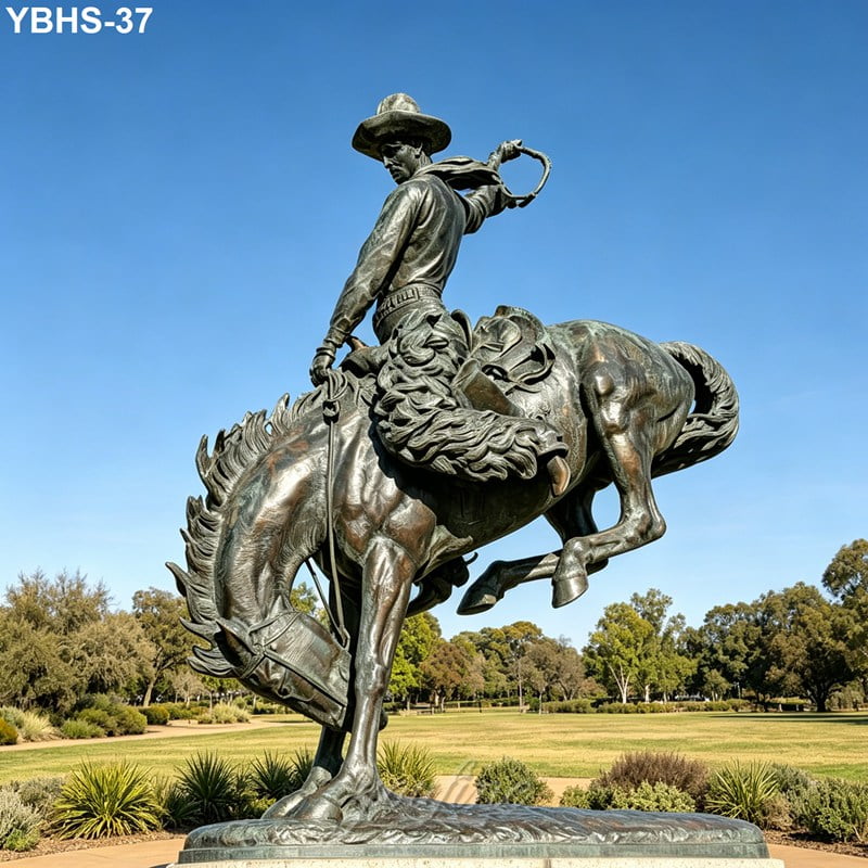 A large bronze sculpture of a cowboy riding a bucking horse, displaying dynamic movement, set in a landscaped park under a clear blue sky.