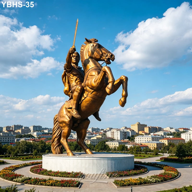 A majestic bronze equestrian statue of a rider holding a sword, rearing on a pedestal surrounded by landscaping, with a city skyline and blue sky in the background.