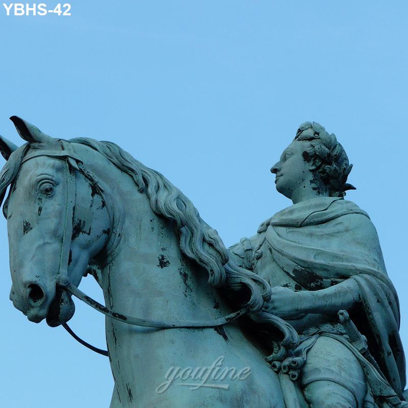 Closeup of a bronze equestrian statue depicting a rider wearing a draped cloak on a horse, with a clear blue sky background.