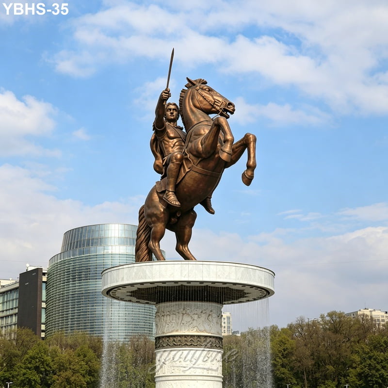 Bronze statue of a rider on a rearing horse holding a sword, atop a decorated circular pedestal with a fountain, set against a cityscape and blue sky.