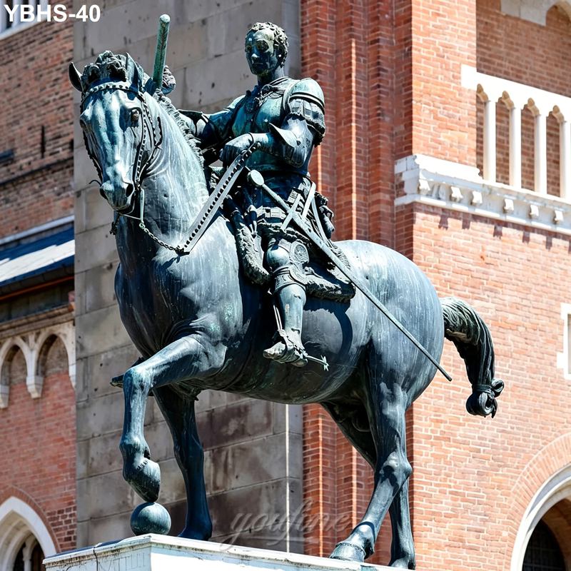 Bronze equestrian statue of an armored knight holding a sword, mounted on a horse, with a historic brick building in the background.