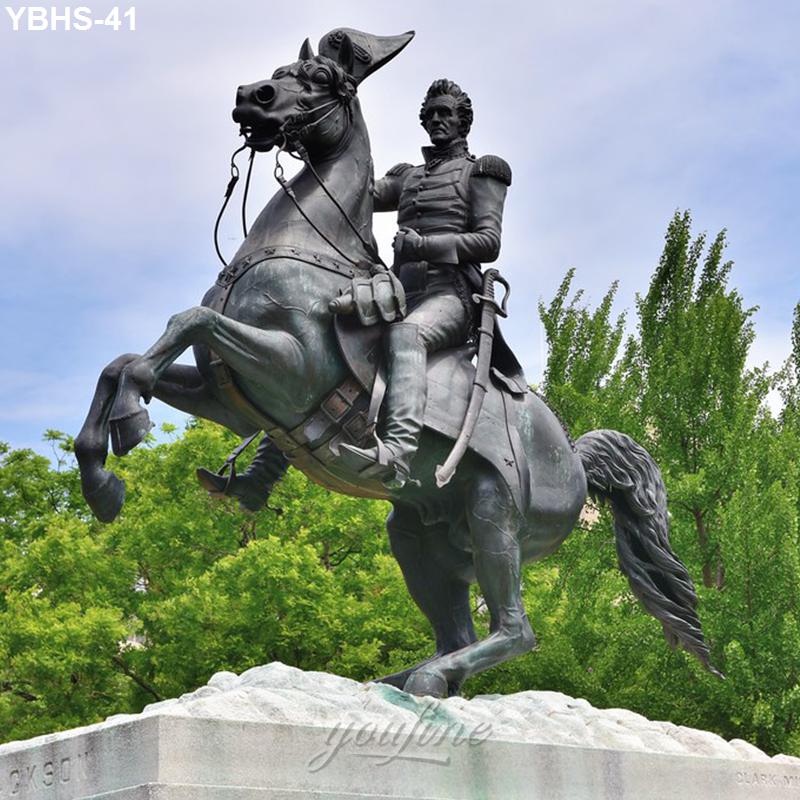 Bronze equestrian statue depicting a rider on a rearing horse atop a pedestal, surrounded by green trees and a blue sky.