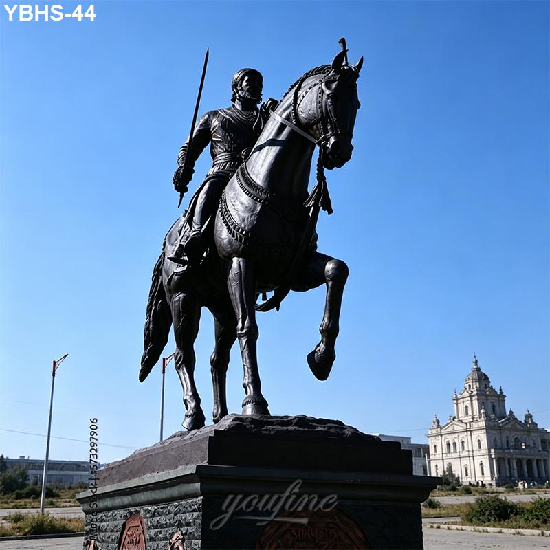 A bronze equestrian statue of a rider holding a sword, mounted on a horse, with a historic building visible in the background under a clear blue sky.