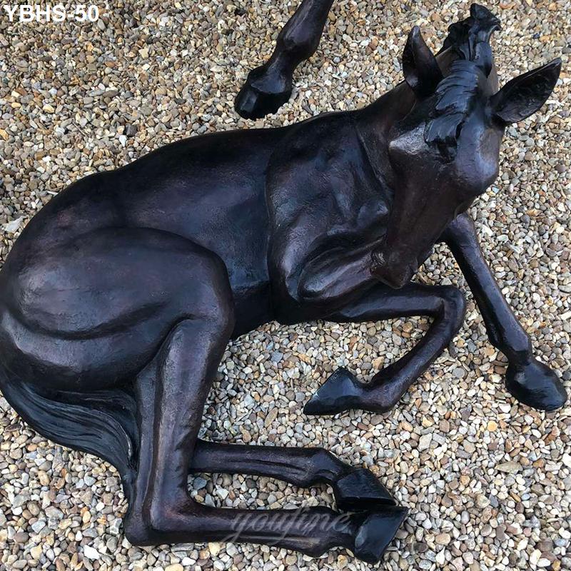 Bronze sculpture of a resting foal lying on a bed of pebbles, showcasing detailed craftsmanship and lifelike features.