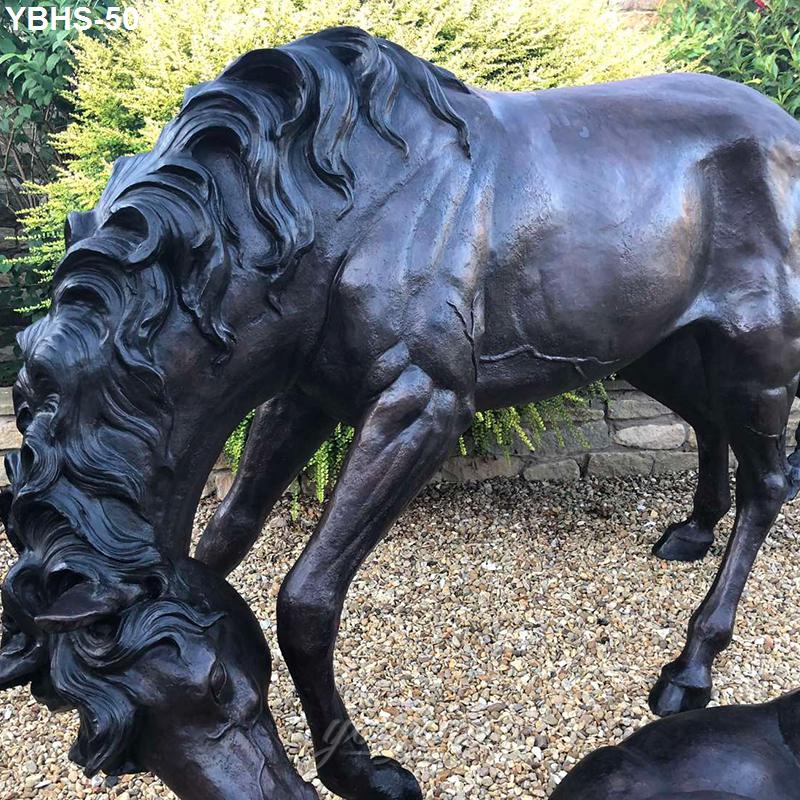 Bronze horse statue depicting a grazing horse with detailed mane and musculature, positioned on gravel near greenery.