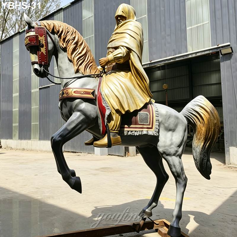 Bronze sculpture of a hooded rider on a rearing horse with intricate golden details, on display outside a metal workshop.