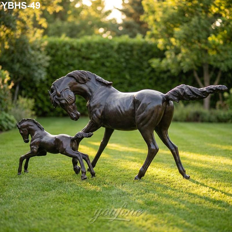 Elegant bronze sculpture of a horse and foal interacting, set on a lush green lawn with trees in the background.