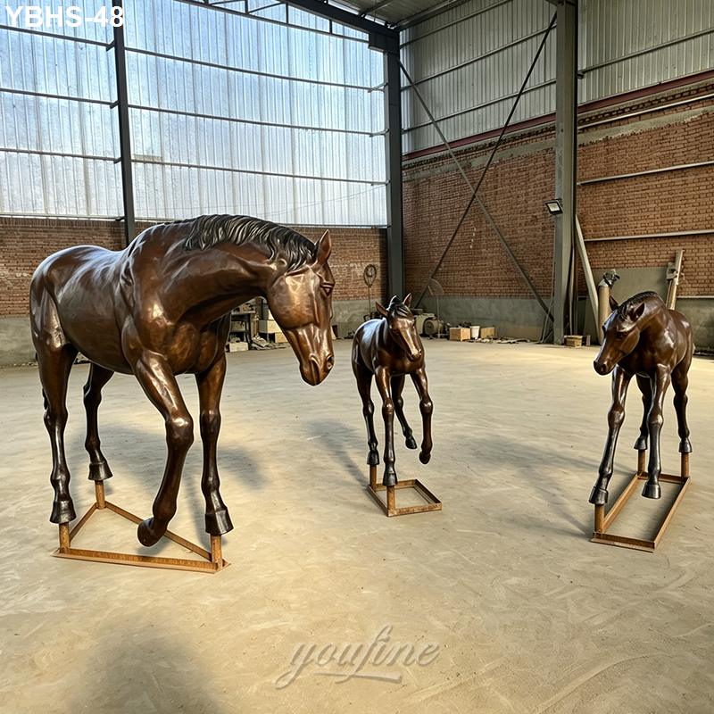 Bronze horse and two foals sculptures displayed indoors in a spacious workshop with industrial brick walls and wide windows.