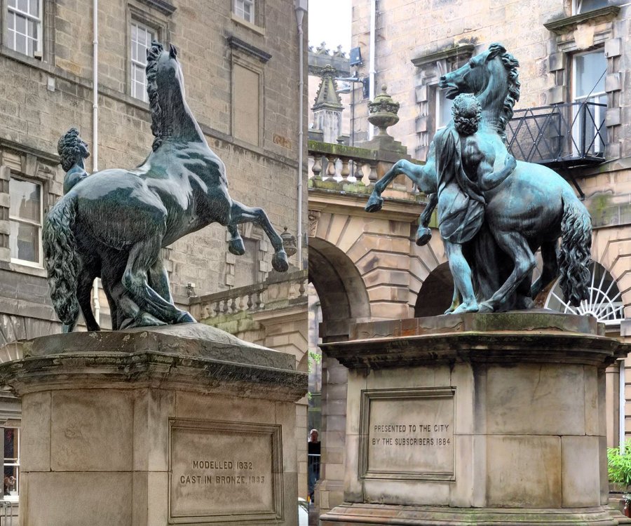 Bronze statue depicting a human figure interacting with a rearing horse, set on a stone pedestal with engraved text, in a city architectural setting.
