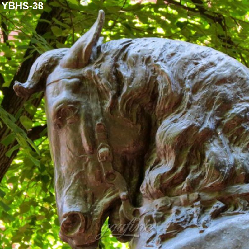 Close-up view of a bronze horse head sculpture with intricate details, set against vibrant green foliage in natural light.
