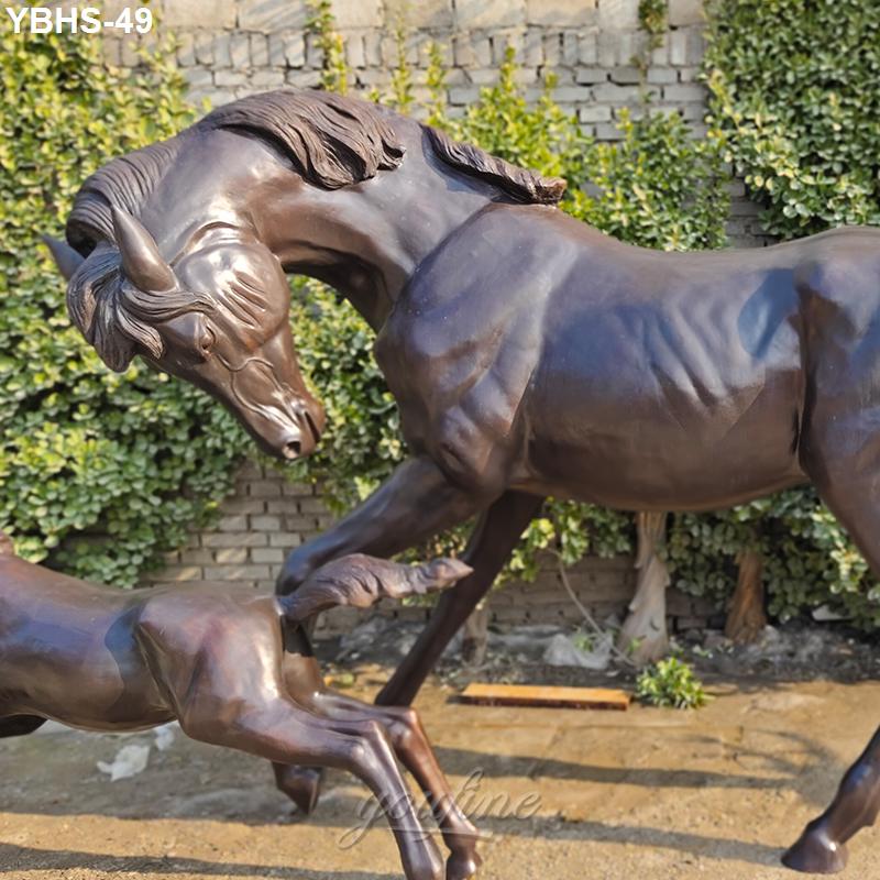 A bronze sculpture depicting a mare and her foal outdoors against a green ivy and brick wall background.