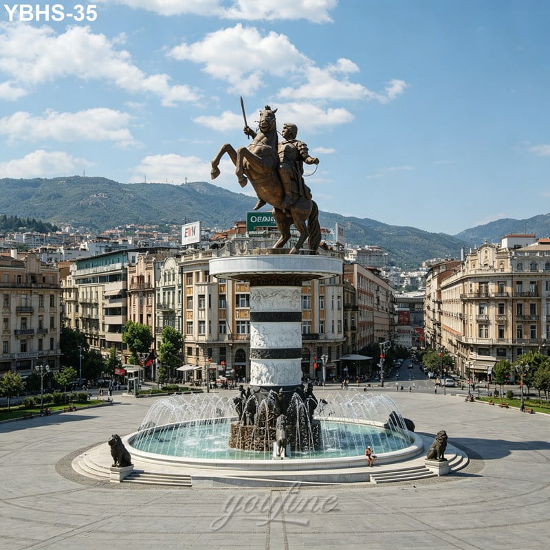 Bronze statue of a horse and rider on a tall column above a fountain in a city square, surrounded by historic buildings and mountains.