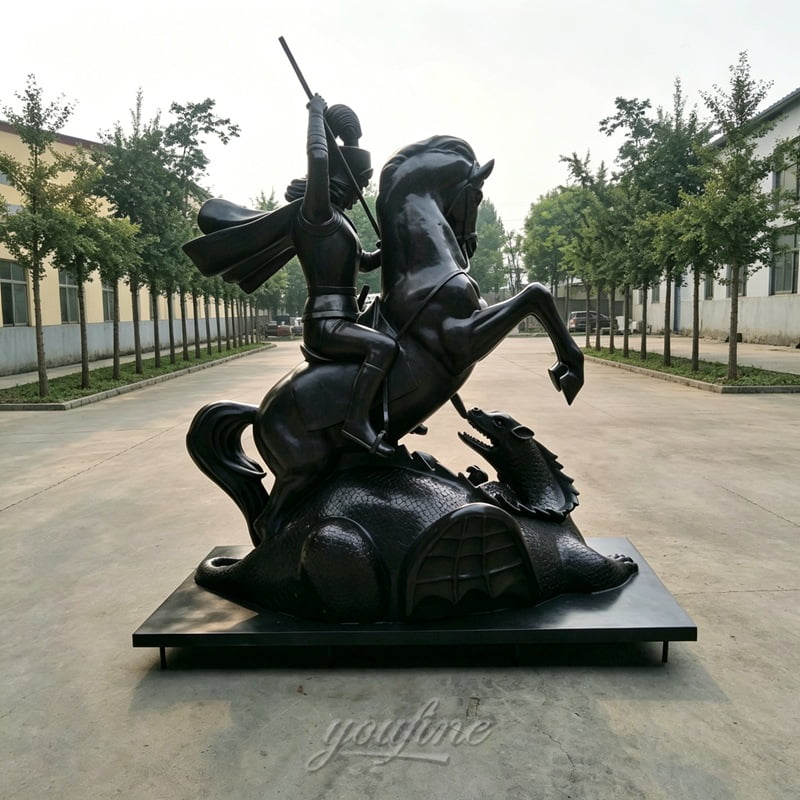 A majestic bronze sculpture showcasing a rider on a rearing horse slaying a dragon, placed outdoors along a paved path with trees.