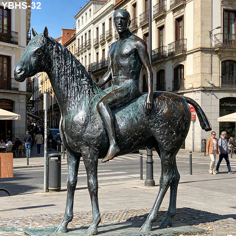 Bronze statue of a horse with a human rider in an urban plaza surrounded by buildings and pedestrians.