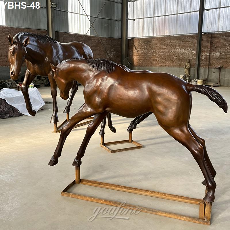 Two bronze horse sculptures with lifelike details displayed on a gallery floor, surrounded by industrial-style walls.