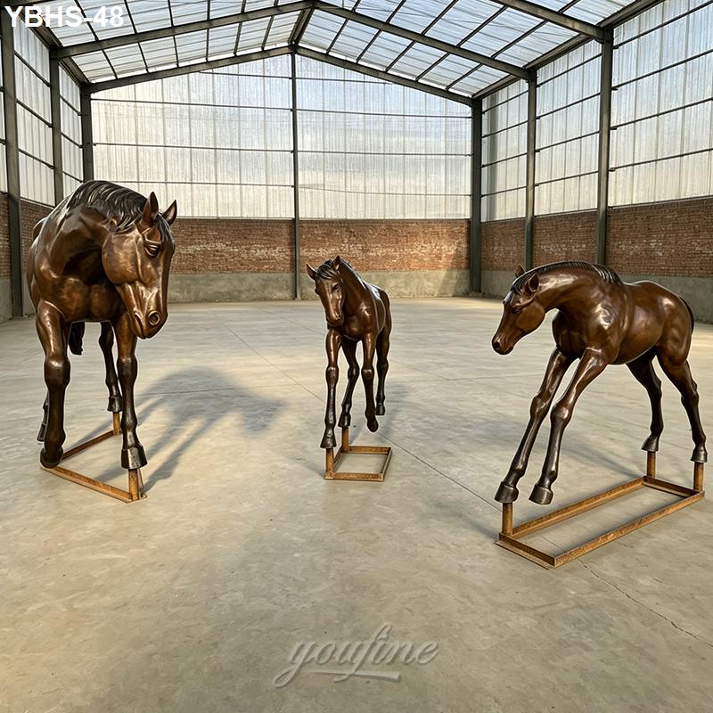 Three bronze horse sculptures, showcasing lifelike details and elegant postures, displayed in a spacious warehouse with brick walls and metal framing.