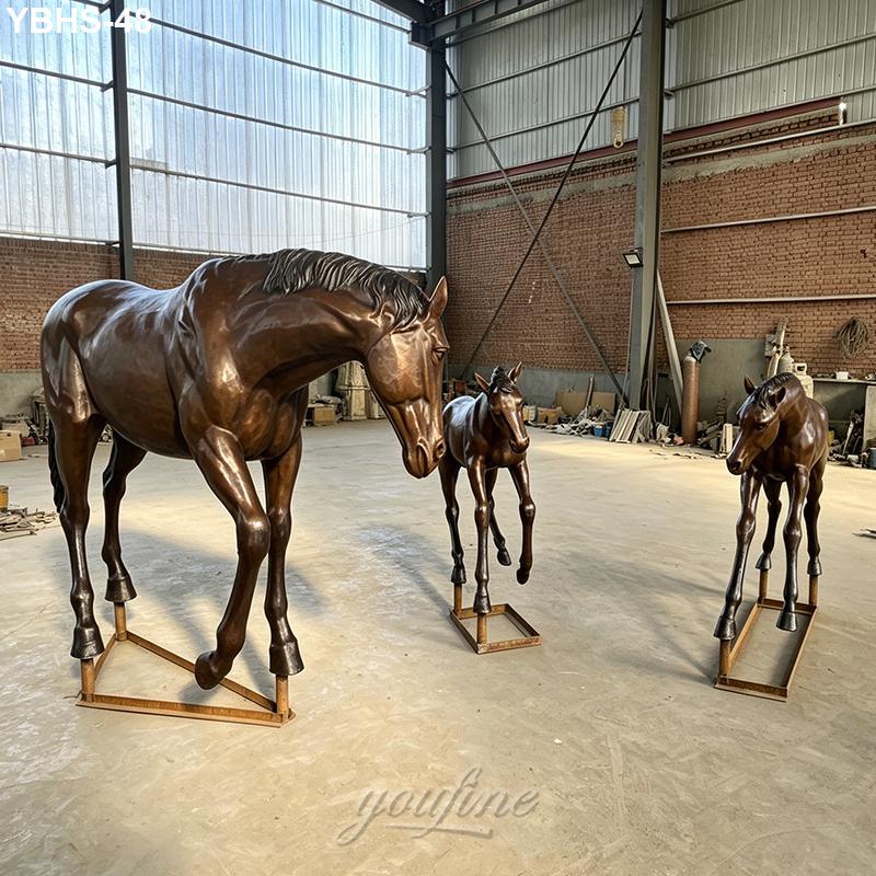 Three intricately crafted bronze horse sculptures, including a mare and two foals, displayed in a spacious workshop with industrial decor.