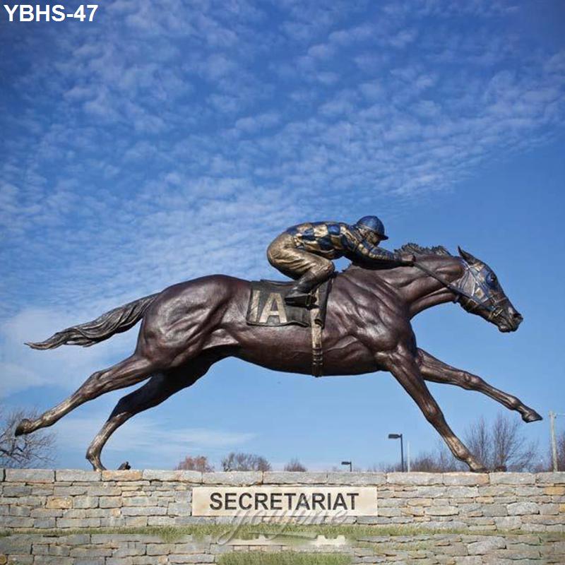 Bronze statue of famed racehorse Secretariat with jockey leaning forward, displayed on a stone base under a blue sky.