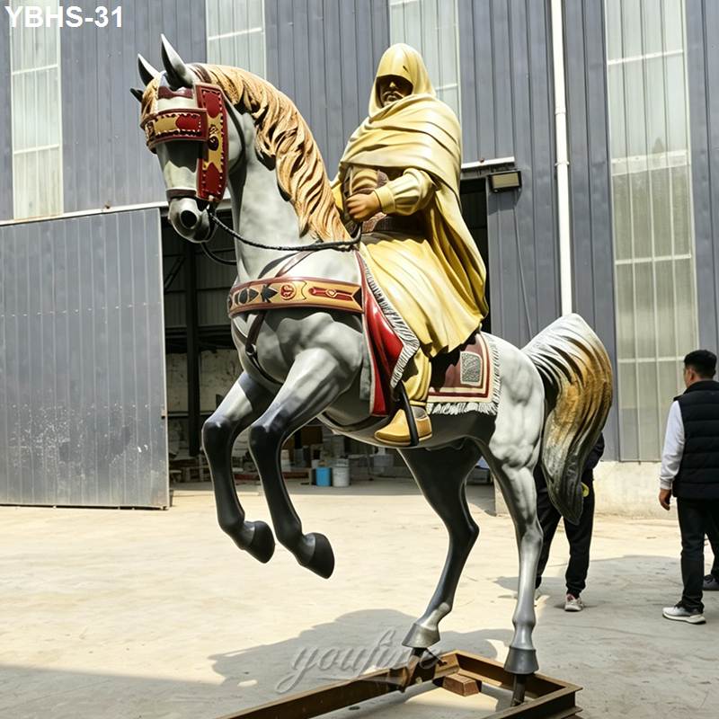 A detailed bronze horse statue featuring a golden-cloaked rider, displayed outdoors near a building with industrial elements.