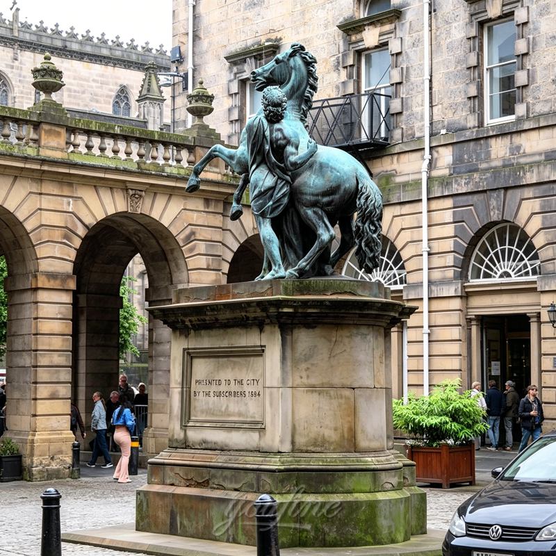 A bronze horse statue with a rearing horse and a rider, placed on a stone pedestal, surrounded by historic architecture.