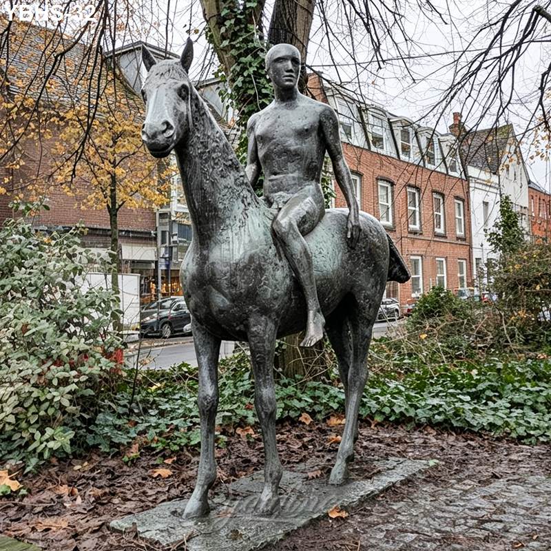 Bronze statue of a horse with a rider depicted sitting peacefully, surrounded by greenery and cobblestone in an urban garden.