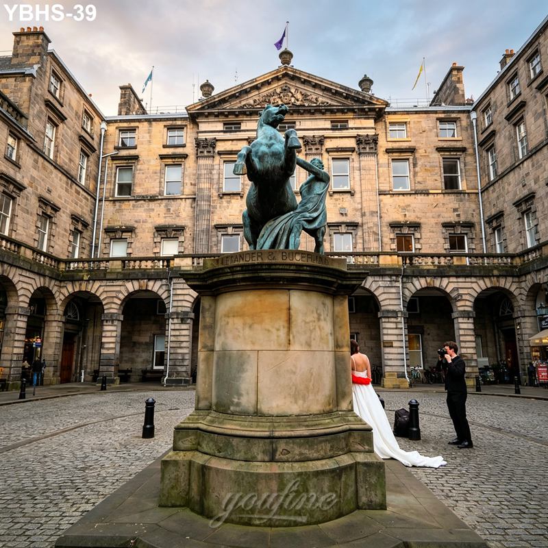 Bronze rearing horse statue on a pedestal in a historic courtyard, with a couple in wedding attire posing for a photographer nearby.
