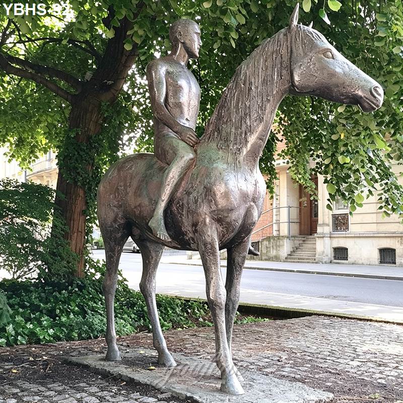 Bronze sculpture featuring a nude rider seated on a horse, set in a paved area with greenery and urban buildings in the background.