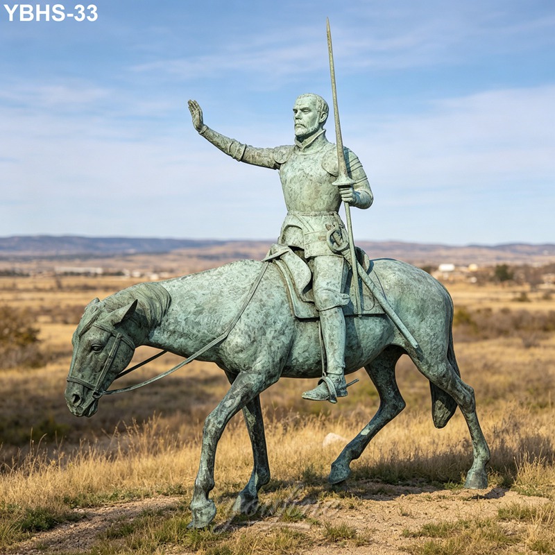 Bronze statue of a knight in armor holding a spear, mounted on a horse, set against the backdrop of an open field under a blue sky.
