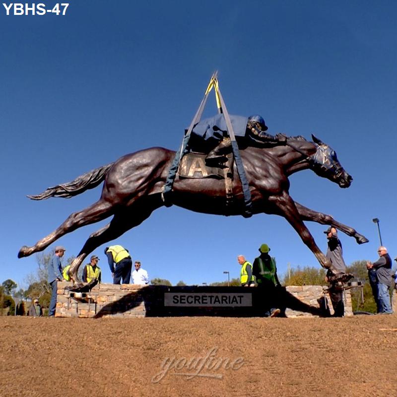 Large bronze statue depicting Secretariat being installed on a base by workers. Figure shows jockey riding horse mid-race.