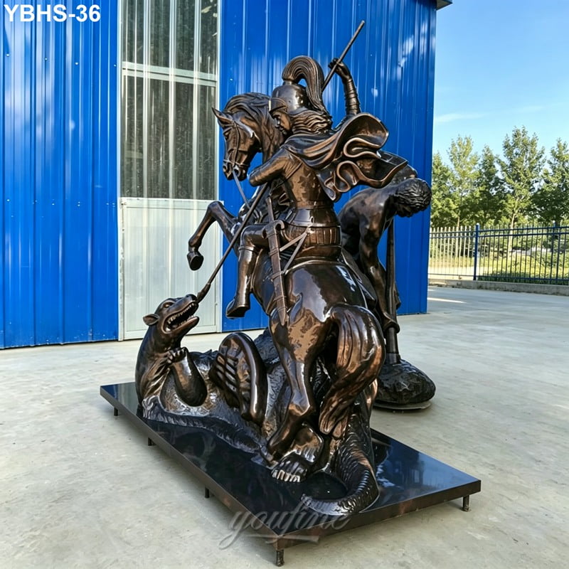Bronze statue depicting St. George on horseback slaying a dragon, set on a solid base with a bright blue building and outdoor setting.