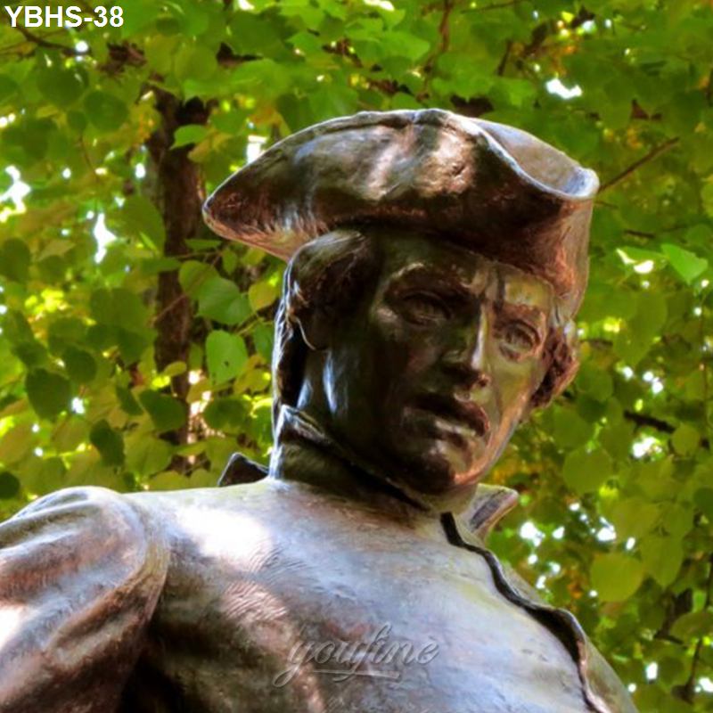 Bronze statue depicting a figure wearing historic attire and a tricorn hat, set against a leafy green background.