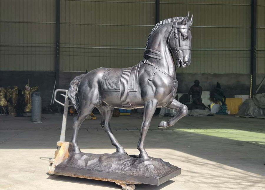 A finely crafted bronze standing horse sculpture with elegant details and mounted on a sturdy base, displayed in a workshop environment.