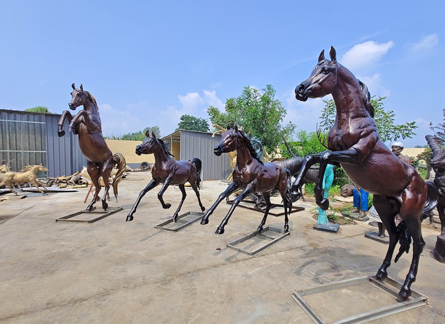 A collection of life-sized bronze horse statues in various dynamic poses displayed outdoors against a blue sky.