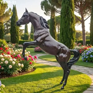 A bronze statue of a Arabian horse positioned in a landscaped garden surrounded by colorful flowers, trees, and a curving stone pathway.