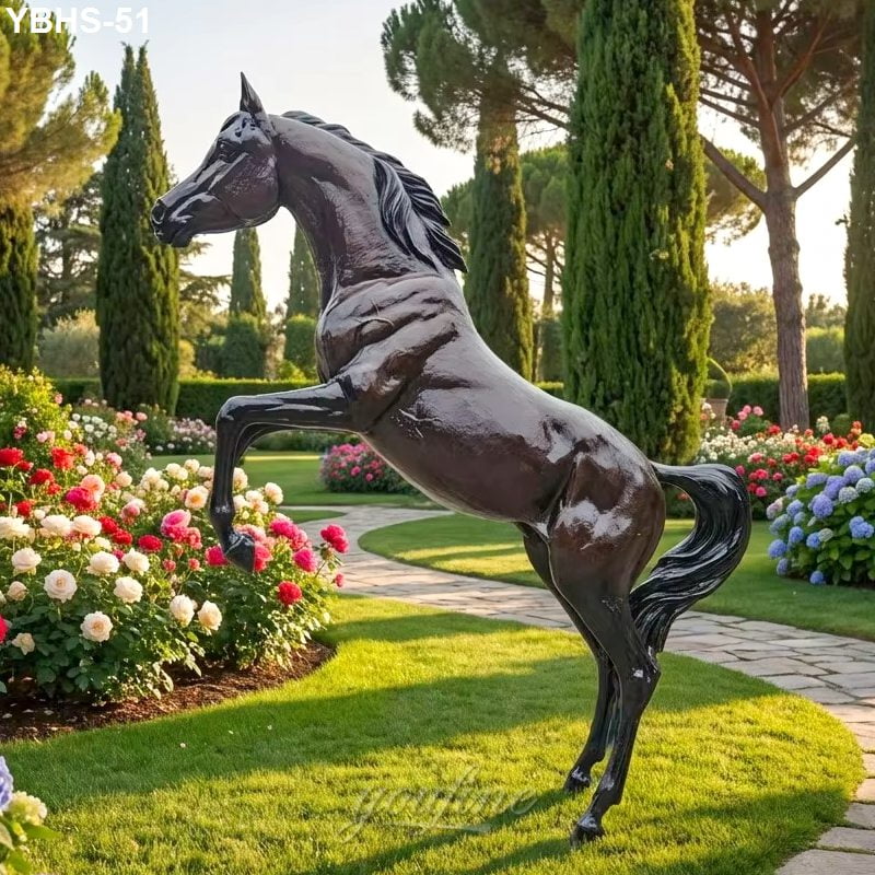 A bronze statue of a Arabian horse positioned in a landscaped garden surrounded by colorful flowers, trees, and a curving stone pathway.