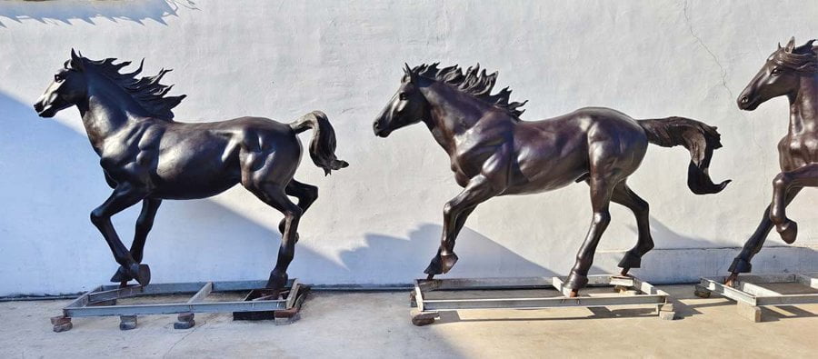 A lineup of three life-sized bronze horse sculptures depicting dynamic running poses, displayed against a white wall.